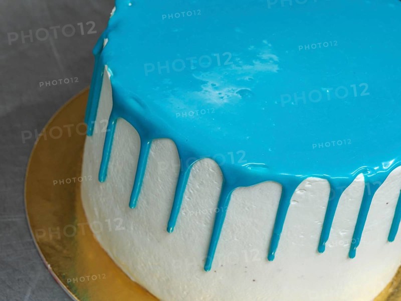 A white frosted cake with vibrant blue icing dripping down the sides on a gold base