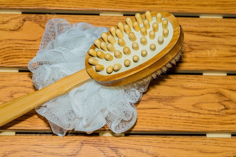 Bath and massage brush and white scrubbing pouf bath sponge on wood grain background