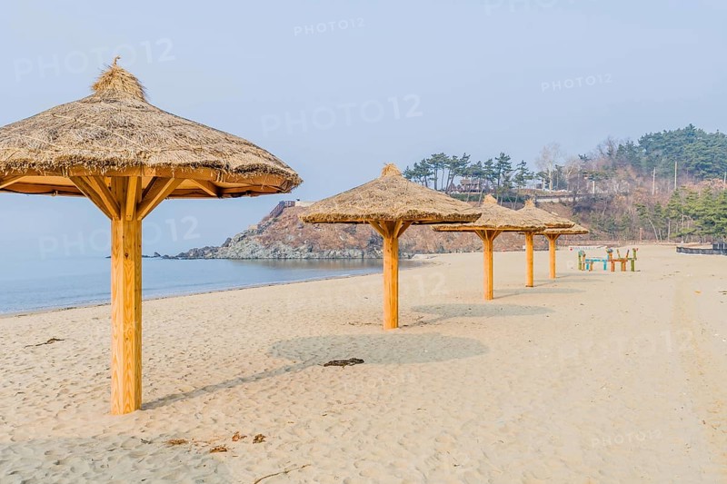 Thatched covered shade pavilions on empty beach under gray winter sky