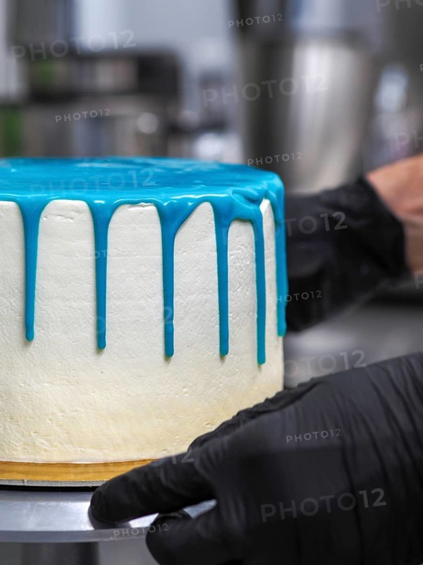 A pastry chef applying blue icing on a white cake, highlighting the baking process in a kitchen