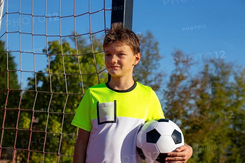 Symbolic image: Ten-year-old boy on a football pitch proudly holding a football in his arms