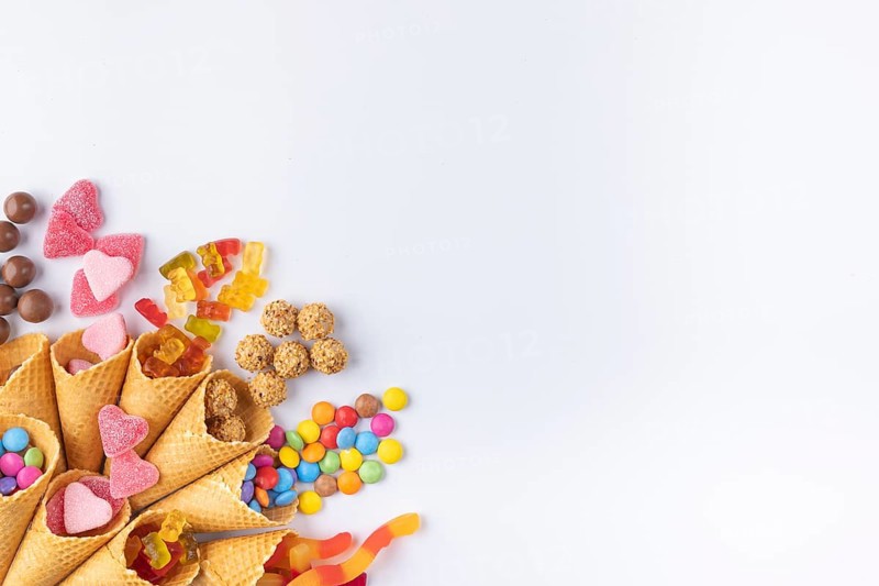 Colourful sweets, gummy bears, chocolate lentils falling out of ice cream cones, copy room, white background