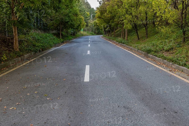 Rural two lane paved road lined with lush foliage in countryside with CCTV cameras in distance in South Korea