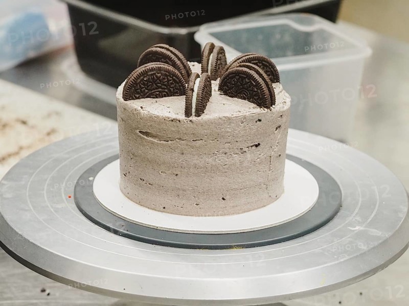 Dark chocolate cookies topping a cream cake with whole Oreos on top, on a kitchen turntable