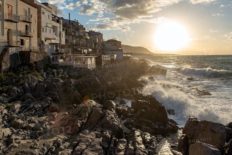 Sea water crashes against the cliffs of the rugged coastline in the town of Cefalu, Sicily, Italy, Europe