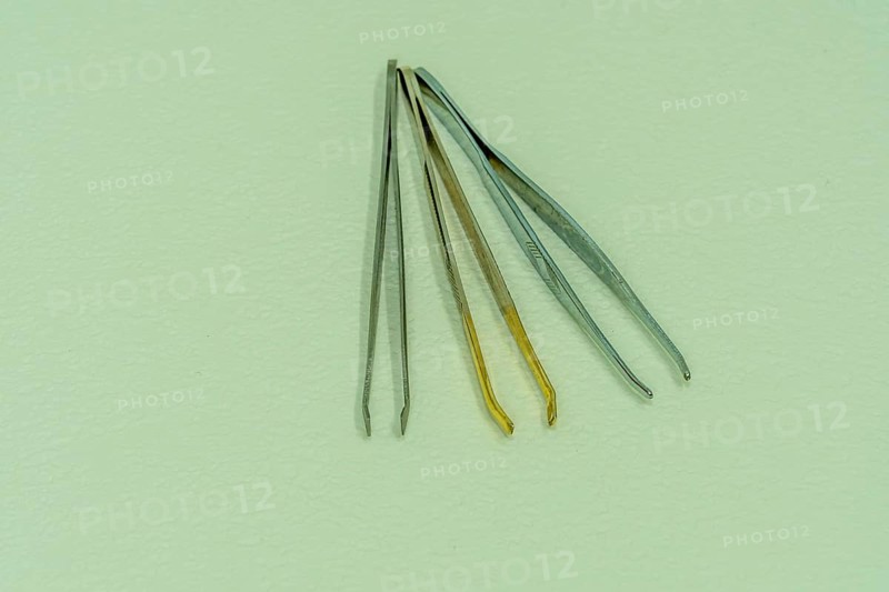 Three pair of tweezers side by side isolated on light textured background