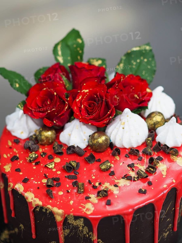 A cake decorated with red glaze, red roses, and chocolate pieces