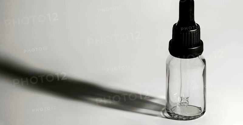 Closeup of single eye dropper bottle with strong dark shadow on white background