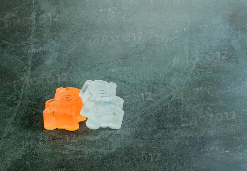 One orange, one white homemade bar of soap made to resemble toy bear on black textured background
