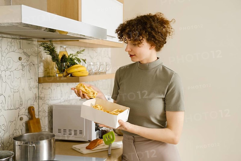 Young woman holding pappardelle pasta in hands over the pot with boiling water