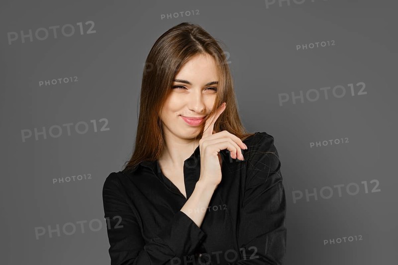 Playful young woman winking with tricky smile on grey studio background