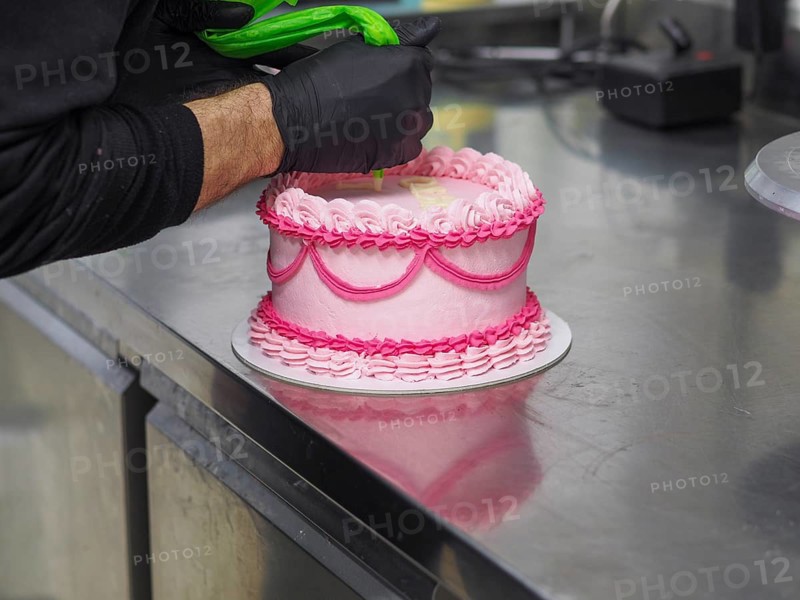 Decorating with text mesagge the top of pink cake with intricate icing patterns using a pastry filling bag