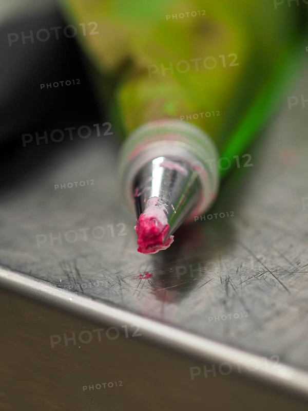 Close-up of a piping pastry bag tip with a bit of pink icing on it, resting on a metal surface