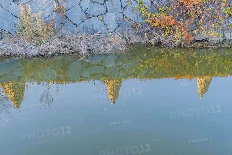 Three Rock cairn on edge of canal reflected in calm blue water in South Korea