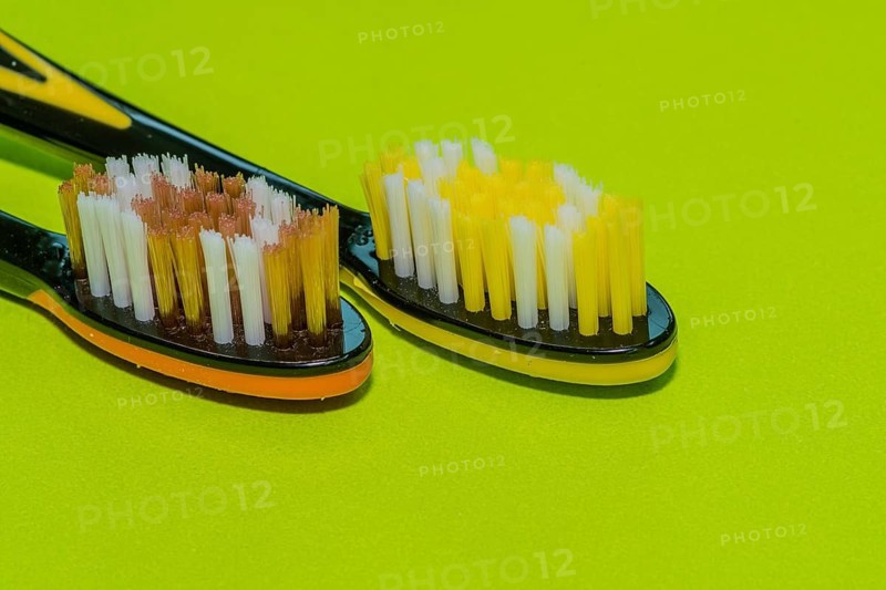 Closeup of two toothbrushes in orange and yellow on a green background