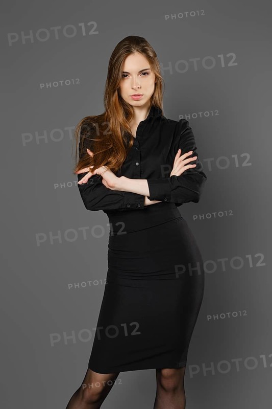 Serious young woman in black blouse and skirt with folded arms