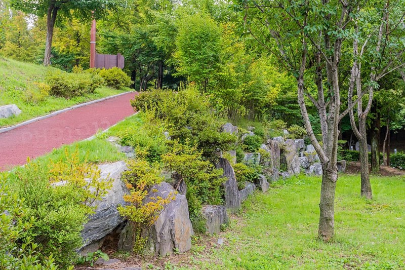 Walking path going uphill behind wall of large boulders in lush urban public park in South Korea