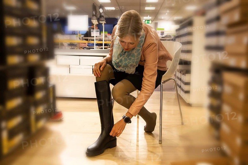 Elegant young woman trying on knee-high black boots in a shop