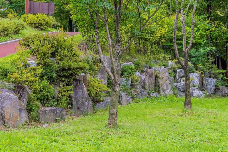Wall of large boulders in lush urban public park with walking path going uphill in background in South Korea