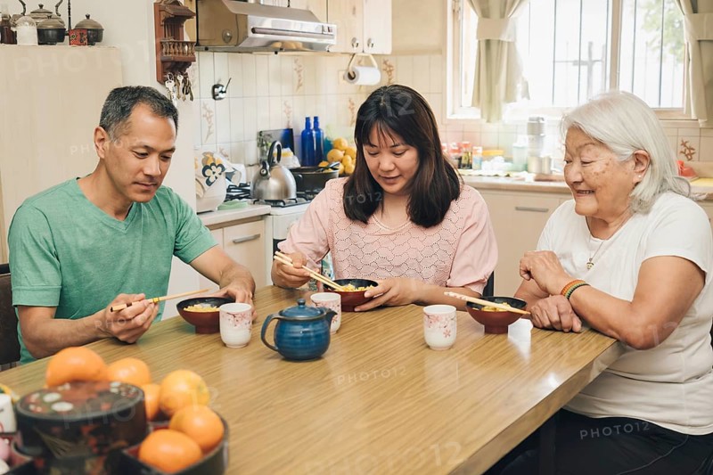 Japanese adult family eating rice with chopsticks. White-haired elderly mother enjoys watching her grown children sharing Japanese typical lunch
