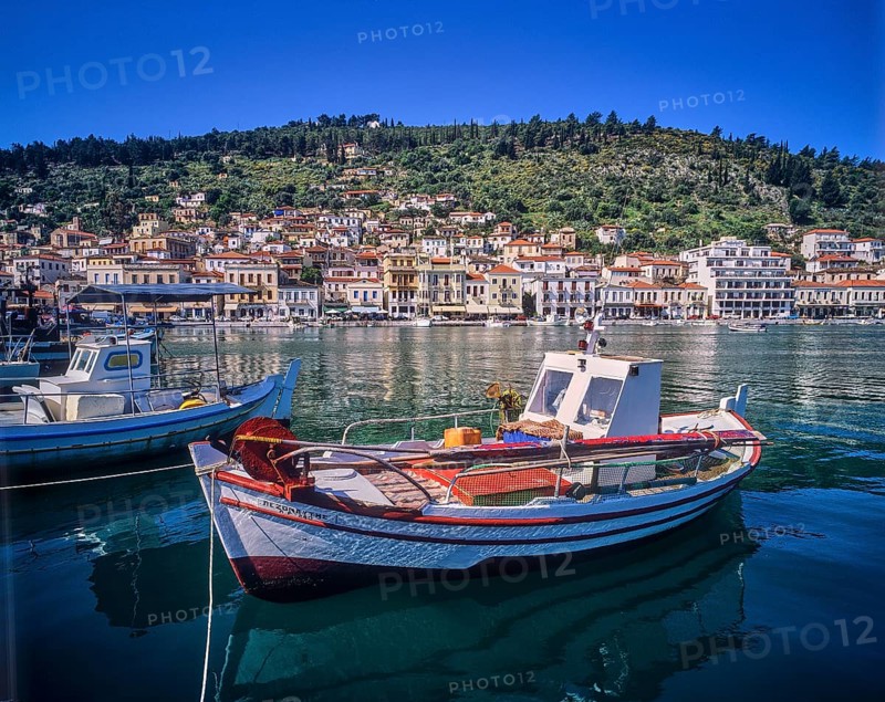 Small boats in the calm harbour water with mountain and city view in the background, Gythio, Mani, Peloponnese, Greece, Europe