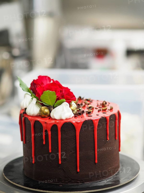 A luxurious chocolate cake with vibrant red icing and roses on a revolving cake stand