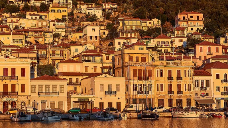 The warm colours of the evening sun shine on the traditional buildings and boats on the coast, Gythio, Mani, Peloponnese, Greece, Europe