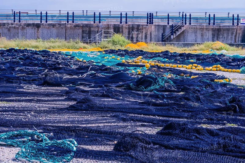 Large fishing nets laid out to dry in gravel lot in front of sea wall on cloudy day in South Korea