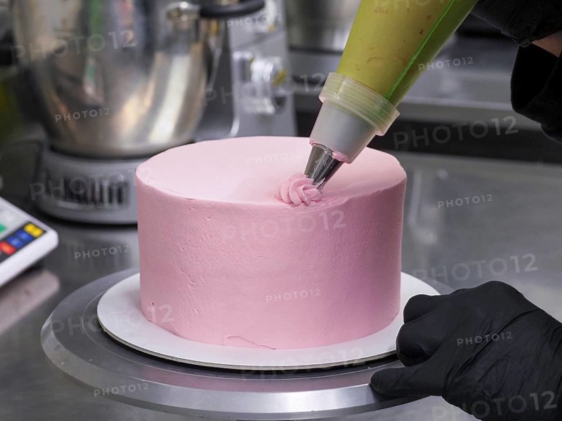 Confectioner with black gloves icing a pink cake with a pastry bag in a precise manner