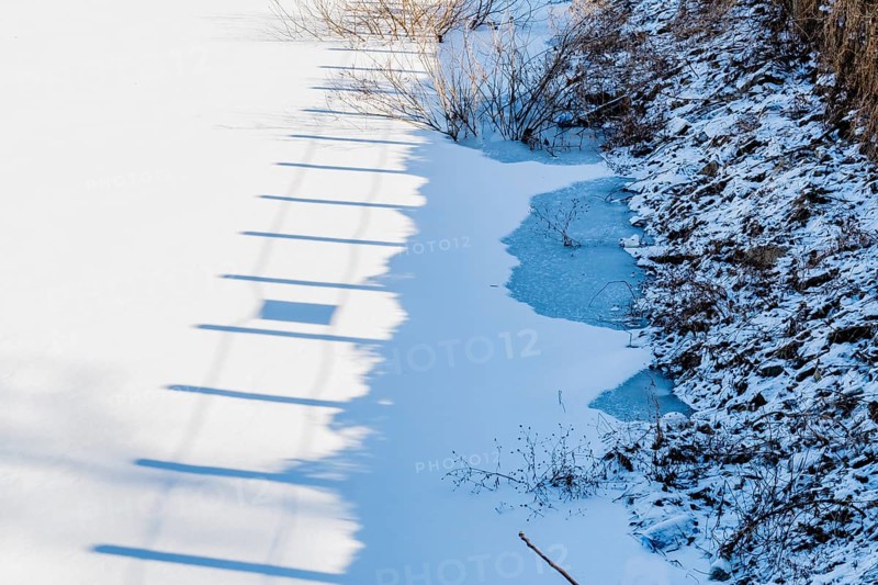 Shadow of wooden fence posts on white surface of frozen lake near shoreline in South Korea