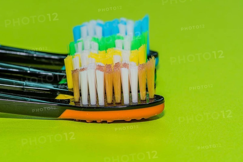 Closeup of four toothbrushes in orange, yellow, green and blue on a green background