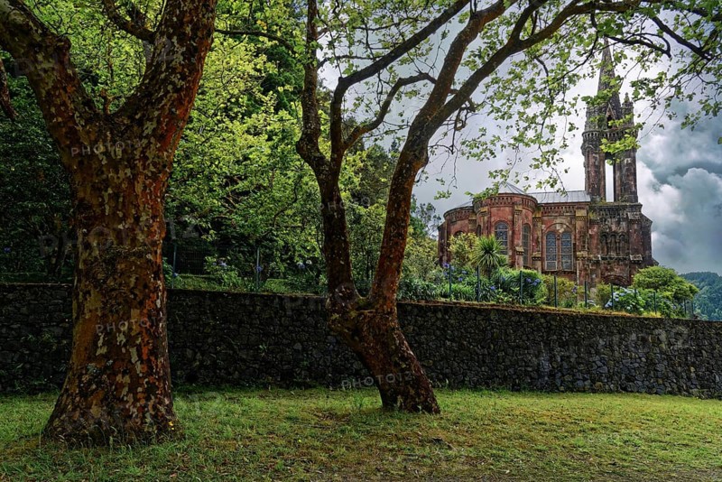 Hidden Gothic church Capela de Nossa Senhora das Vitorias behind trees and an old stone wall in a quiet green area, Furnas Lake, Furnas, Sao Miguel, Azores, Portugal, Europe