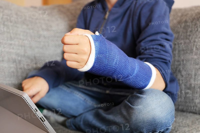 Boy with arm in plaster sits on the sofa with a tablet