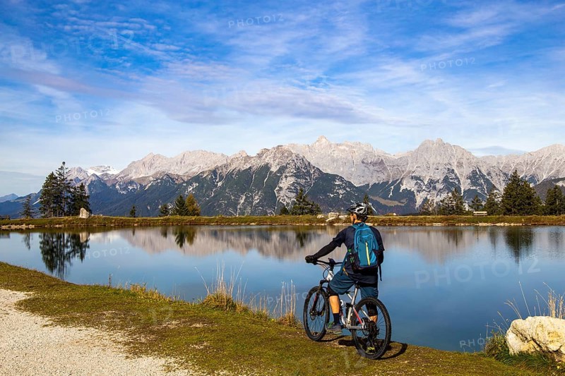 Mountain biker taking a break at the Kaltwassersee lake in Seefeld/Tyrol. The snow-covered peak on the left of the picture is the Zugspitze