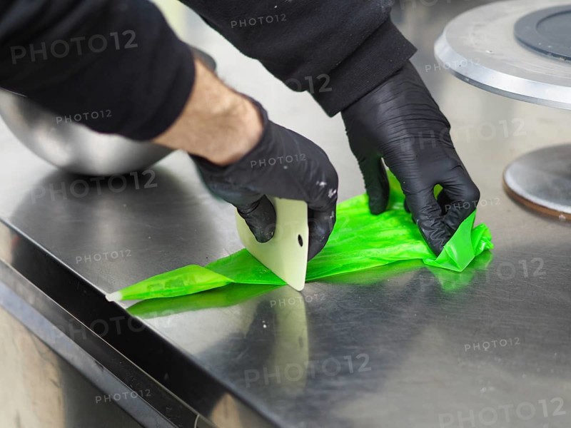 Pastry chef preparing a filling pastry bag with vibrant green frosting in a commercial kitchen