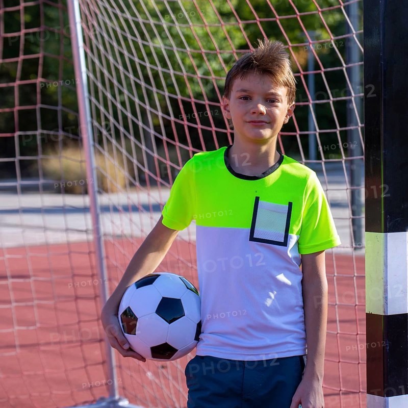 Symbolic image: Ten-year-old boy on a football pitch proudly holding a football in his arms