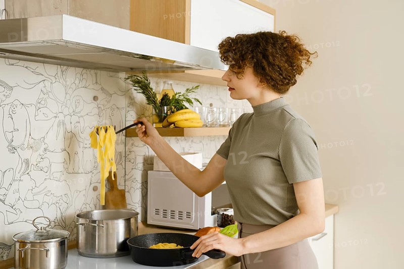 A woman takes out cooked pasta from a pot of water