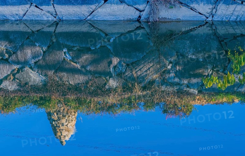 Rock cairn on edge of canal reflected in calm blue water in South Korea