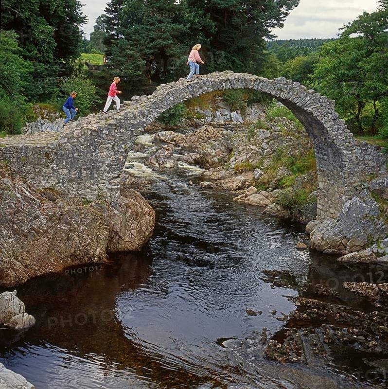 Three women walk across the packhorse bridge at Carrbridge in Scotland, Great Britain, Europe. Scanned 6x6 slide