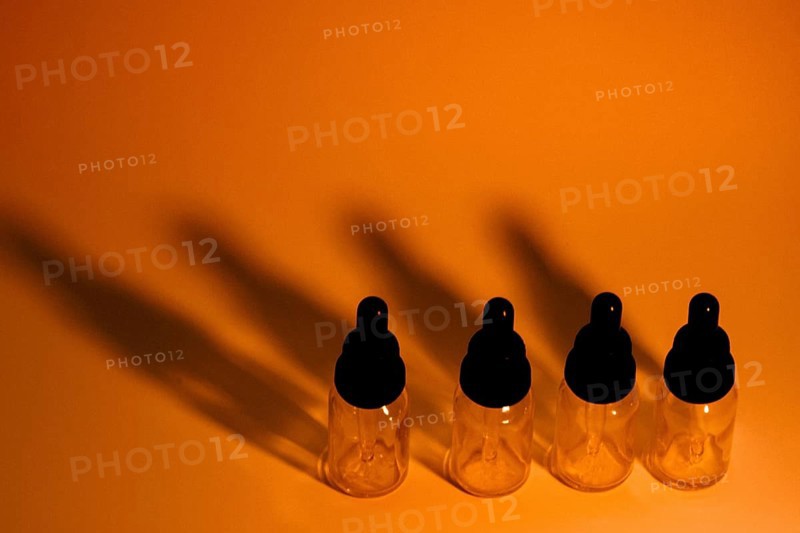 Four glass eye dropper bottles with dark black shadows on golden orange background. A little noise added for effect