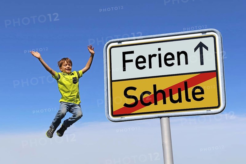Symbolic image: German town exit sign with the words Schule/Ferien. In the background, a boy is jumping for joy (composing)