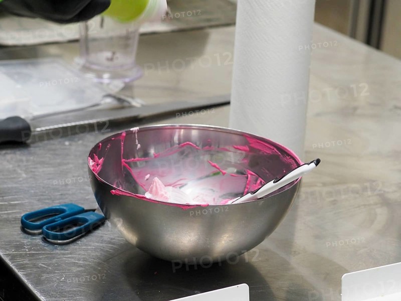 A mixing bowl with remnants of pink icing and a spatula on a kitchen counter