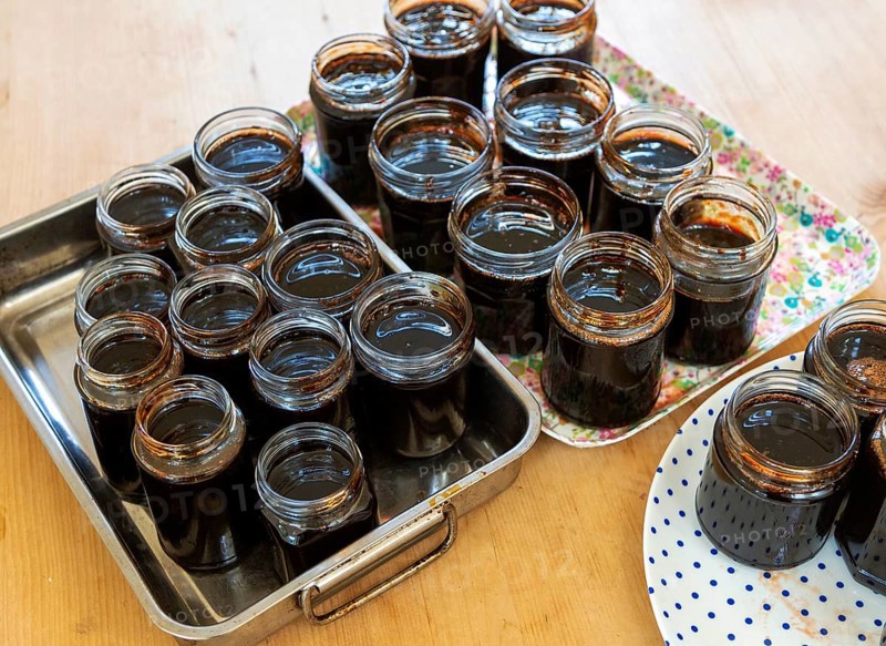 Open topped jam jars filled with setting dark liquid quince jam jelly homemade conserve