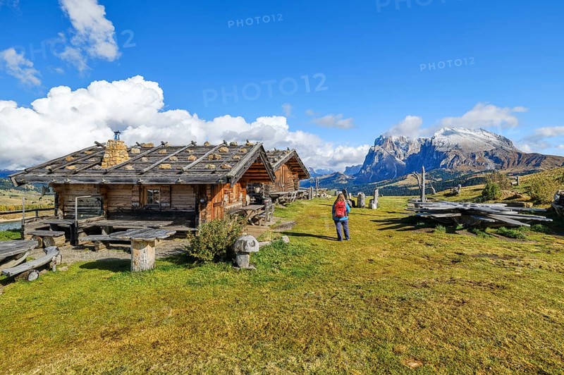 Edelweiss hut on Alpe di Siusi, hiker with red rucksack, Sassopiatto and Sassolungo, clouds, Dolomites, South Tyrol
