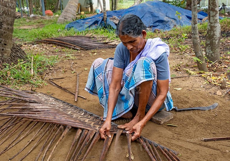 A village woman demonstrates the traditional craft of making mats from coconut leaves using her toes, Kerala Backwaters, Kerala, India, Asia