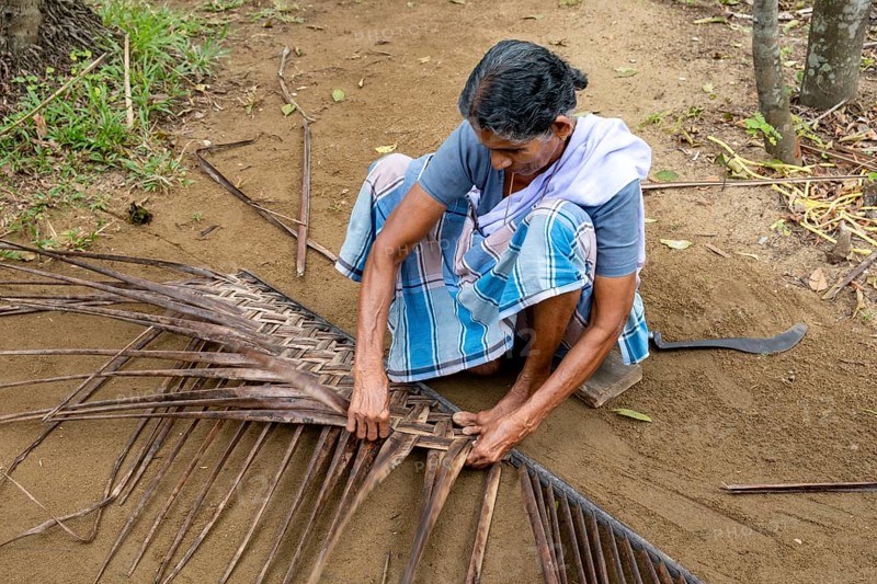A village woman demonstrates the traditional craft of making mats from coconut leaves using her toes, Kerala Backwaters, Kerala, India, Asia