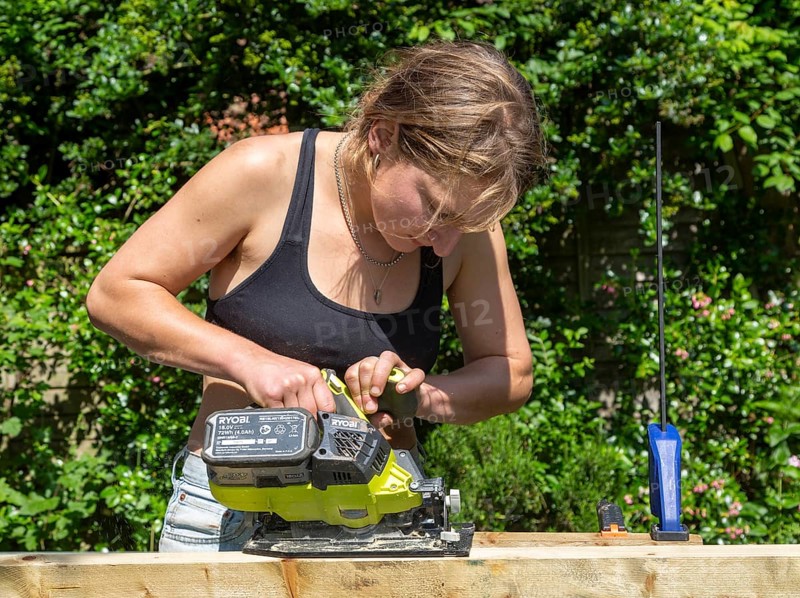 Young woman using electric power sawing tool without safety googles or protective clothing, model released