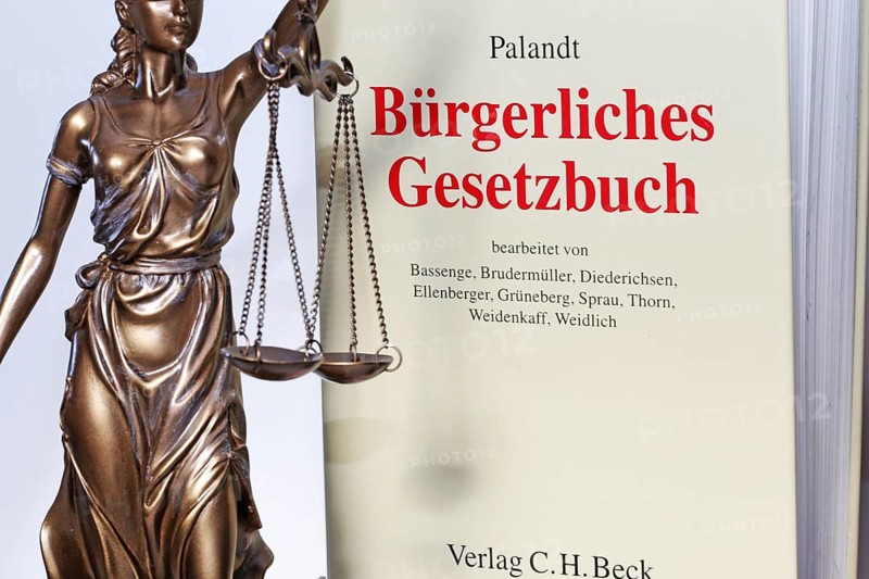 Symbolic image of a court judgement: Justitia with the Palandt (German Civil Code) in the background