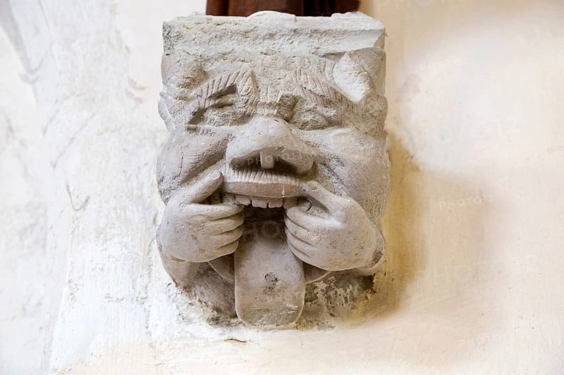 Grotesque corbel stone figure with mouth pulled open and rolling tongue, Church of Saint Nicholas, Hintlesham, Suffolk, England, UK