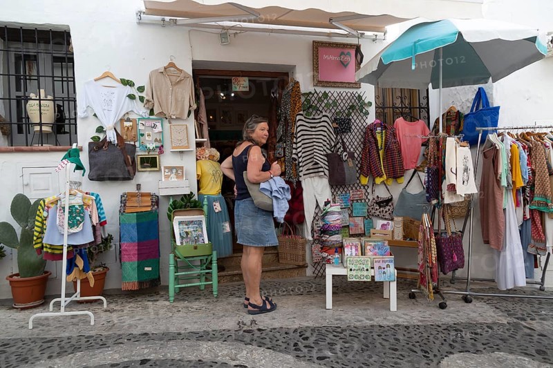 Woman tourist outside souvenir shop, Frigiliana, Axarquia, Andalusia, Spain display of clothes and craftwork